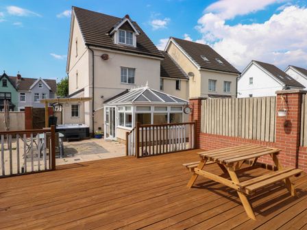 A backyard with a wooden deck and picnic table a conservatory attached to a house and neighboring houses in the background at Alban Road in Llanelli