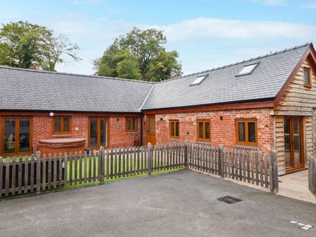 An exterior view of a brick and wood house with multiple windows a hot tub and a fenced yard at The Granary in Llandyssil near Montgomery