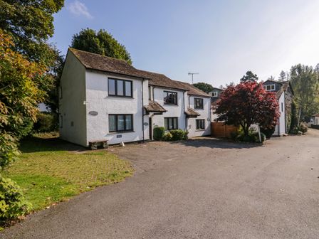 A white two story house with multiple windows and a red tree in front with a driveway at Buttermere in Ambleside