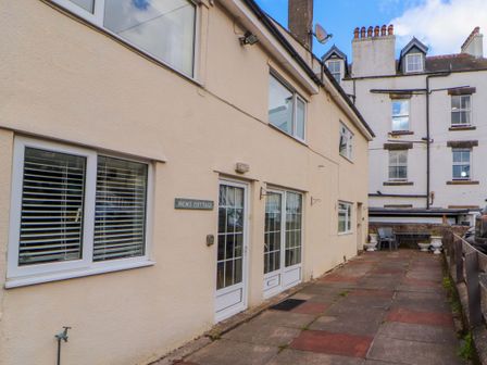 Exterior view of a beige cottage with windows and doors along a paved walkway at Brews Cottage in Keswick