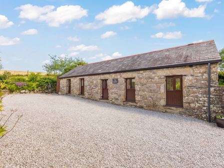 A stone building with three doors and four windows surrounded by gravel and greenery at The Stables in St Neot