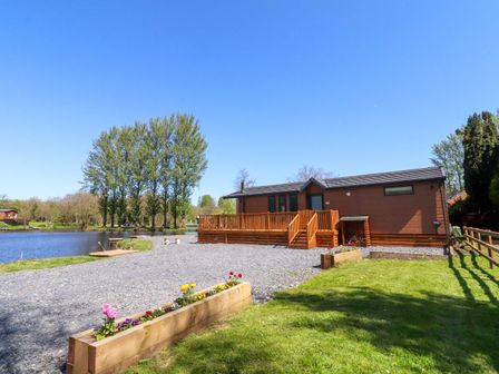 A lodge with a deck by a lake at Lakeside Lodge Bowland Lakes Leisure Village near Garstang
