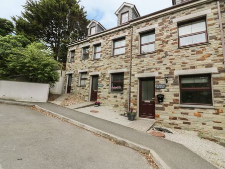 A stone facade building with multiple doors and windows and plants outside at The Beach Hut in Crantock near Newquay
