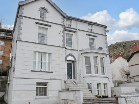 The exterior of a multi-story white building with stairs leading to a black door at Apartment 1 in Llandudno