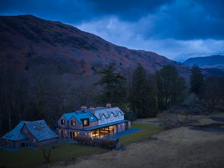 A house with lights on surrounded by trees and hills at Eskdale Retreat in Boot