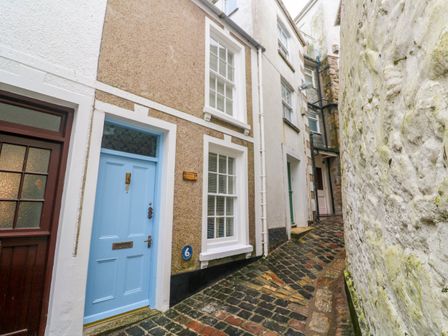 A narrow cobblestone alley with doors and windows on buildings on one side and a white textured wall on the other at Seahorse Cottage in St Ives