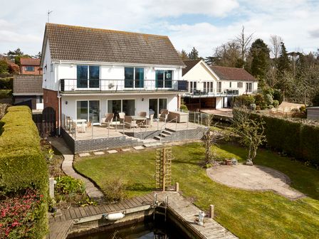 A garden with a patio area and seating behind a two story house with a dock at White Gables in Horning