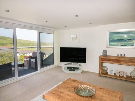 A living room with a wooden table a flat screen tv and a console table with decorations at Atlantic View in Holywell Bay