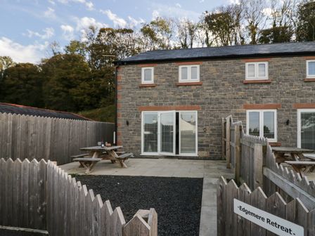 An outdoor patio area with wooden picnic tables and a stone house behind at Edgemere Retreat in Cartmel