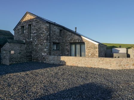 A stone building with a gravel area in front and a stone wall near a grassy hill at Apple Tree Barn Near Dalton-In-Furness