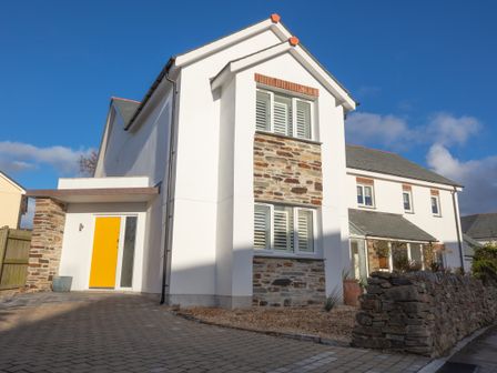 A white two-story house with stone accents and a yellow front door at Sandwood Studios in Crantock