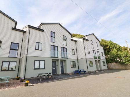 A row of three-story modern townhouses with picnic tables and flower pots outside at 3 Yr Hen Lys in Pwllheli