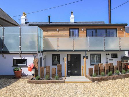 A two story house with wooden and white exterior and frosted glass balcony with a pebble stone front yard at Chapel House in Rhosneigr