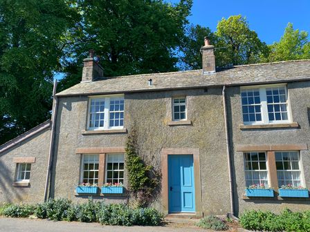 A stone cottage with a blue door and flower boxes on windows surrounded by greenery at Winn's Cottage in Pooley Bridge