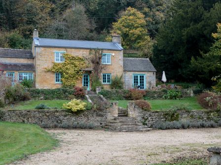 A stone house with blue window frames and doors surrounded by a garden and trees at The Snicket in Turkdean near Northleach