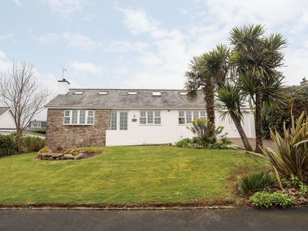 A bungalow with stone and white walls surrounded by a lawn and palm trees at The Palms in Abersoch
