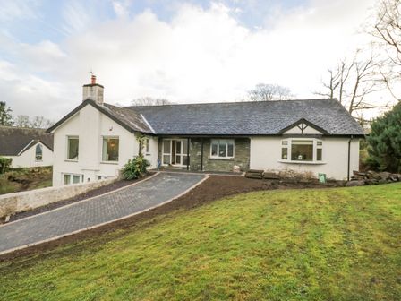 A driveway leading to a single-story house with a pitched roof and white walls at Whimhowe in Windermere