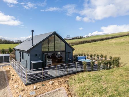 A small modern house with a large glass front and outdoor seating on a deck with a hot tub on a hill at Hares Hill in Thornton Le Dale