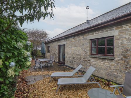 An outdoor patio area with two lounge chairs a table and four chairs next to a stone house at Owl Cottage in Ashen Cross Pelynt