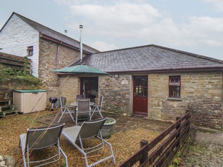 An outdoor patio area with two lounge chairs a table with four chairs an umbrella a storage box and a barbecue grill at Court Cottage Ashen Cross Pelynt