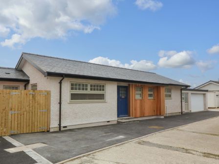 A single-story house with a blue door wooden panels and adjacent garage at Awel-Y-Mor in Trearddur Bay