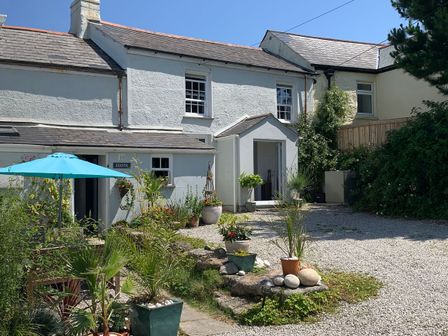 A white two story house with a blue umbrella and potted plants in a gravel yard at Kernyk in Carn Brea near Pool