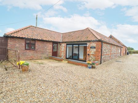 A gravel courtyard with flower pots outside a brick and flint building with a tiled roof at The Old Dairy in Tittleshall near Brisley
