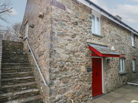 A stone cottage with a red door and stone steps beside it at Wood Cottage in Solva