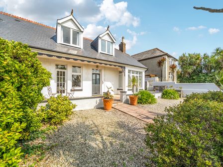 A house with windows and a door surrounded by plants and a gravel pathway at Palm House in Newquay