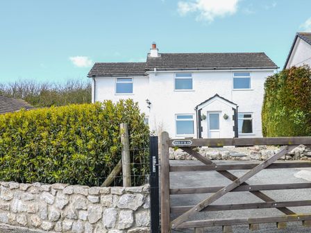 A white two-story house with four windows a front door wooden gate and stone wall at Bryn Uchaf in Benllech
