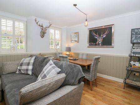 A dining area with a wooden table surrounded by plaid chairs next to a grey sofa with plaid cushions at 1 Boarbank Farm in Allithwaite near Cartmel