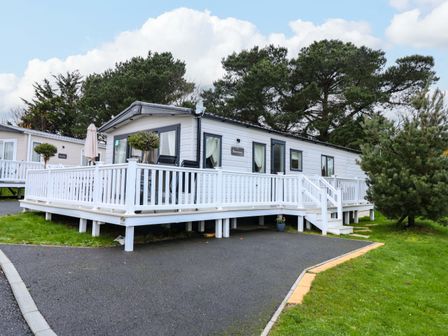 A white static caravan with a ramp and stairs on a paved area surrounded by trees at 117 Crosswinds in Hillway near Bembridge