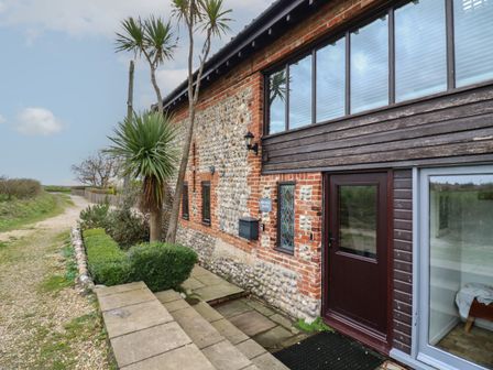 The exterior of a building with stone and brick walls with windows a door and plants along a pathway at Bridge Barn in Sidestrand near Overstrand
