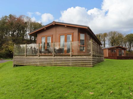 A wooden lodge with glass railing on a grassy hill with trees in the background at Lakeview Lodge in Forton near Garstang
