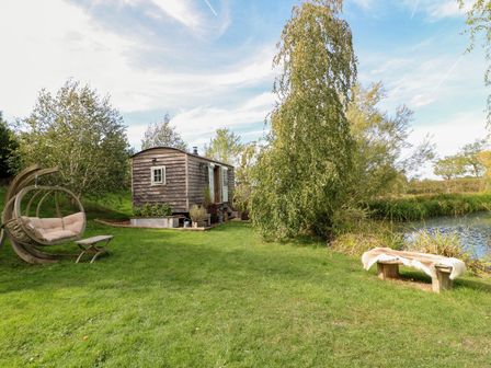 A wooden hut and seating area beside a pond at Herbie's Shepherds Hut at Shepherds Lodge Retreat and Wellness Bottesford near Redmile and Vale of Belvoir
