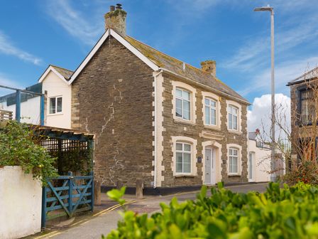 A stone house with white window frames and a blue wooden gate at Captain's Walk in Newquay