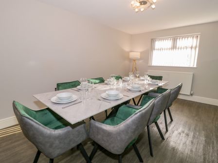 A dining room with a rectangular table set for eight and green and gray chairs at Bwthyn Y Mor in Tal-Y-Bont