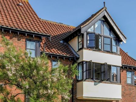 A brick house with a tiled roof and multiple open windows with black frames at 4 Victoria Court in Sheringham