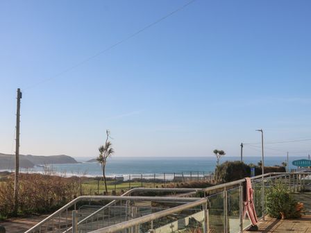 A coastal view with ocean waves palm trees and a metal railing at 5 Fistral Waves in Newquay