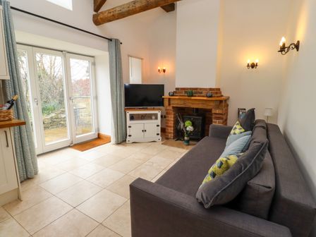 A living room with a gray sofa cushions a TV on a white cabinet a brick fireplace and glass doors at Christon Well Cottage Christon Bank near Embleton