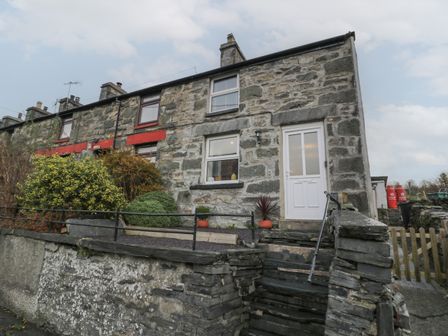 Exterior of a stone terraced house with a white door and windows with bushes in front at Bryn Tawel in Penmachno