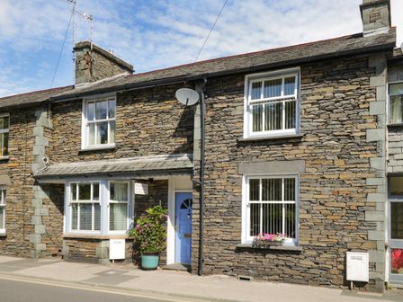 A stone exterior house with a blue door and white windows with flower pots at Two Tweenways Ambleside