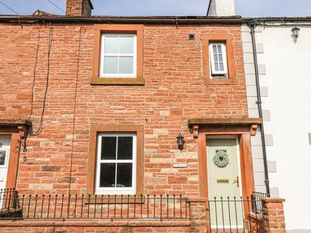 The front exterior of a stone house with two windows a door with a wreath and a metal fence at 3 Eden View in Lazonby