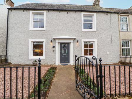 A house with a dark grey front door and four windows surrounded by a black metal gate at 1 Brookside in Warcop