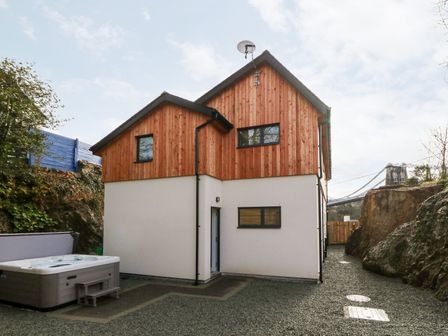 A two story house with wooden paneling and a hot tub outside at Ty Chwarel in Menai Bridge