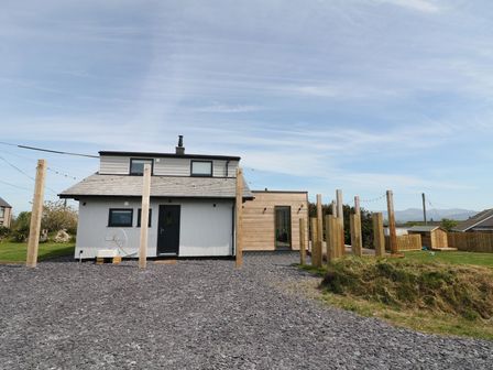 A modern house with wooden posts and gravel driveway at Forest Lodge in Newborough