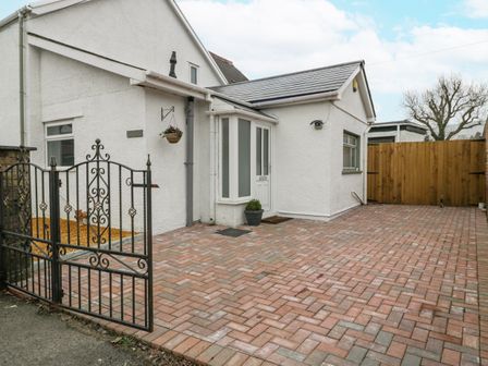 A paved driveway with a black metal gate and a white house with a wooden fence at Meillion in Hirwaun