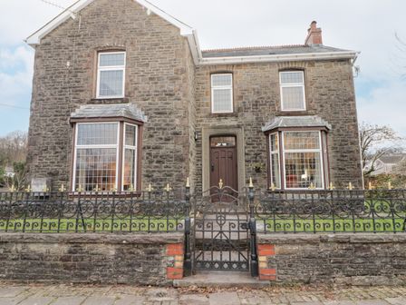 The front view of a stone house with a gate and iron fence at Glan Yr Afon in Ystradgynlais