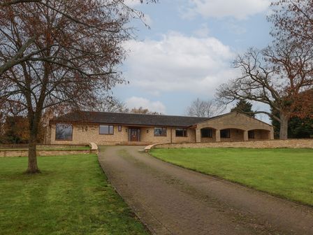 A stone house with a driveway and two large trees on a grassy lawn at Blossom Hill near Witney
