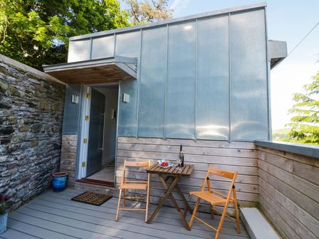 A small outdoor patio with a wooden table, two chairs, a bottle of drink, and a bowl of strawberries outside a building with stone and metal walls at Harbour Heights in Dartmouth